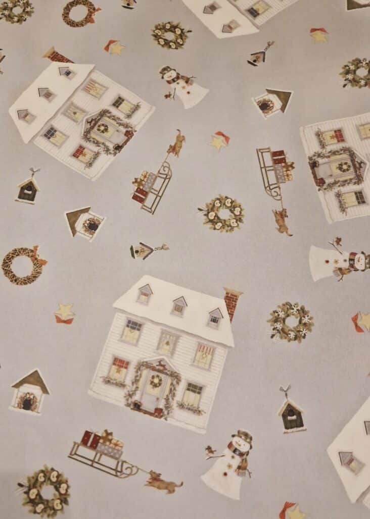 Christmas wrapping paper featuring a festive scene with snowmen, sledges, wreaths and a snow-covered Christmas house